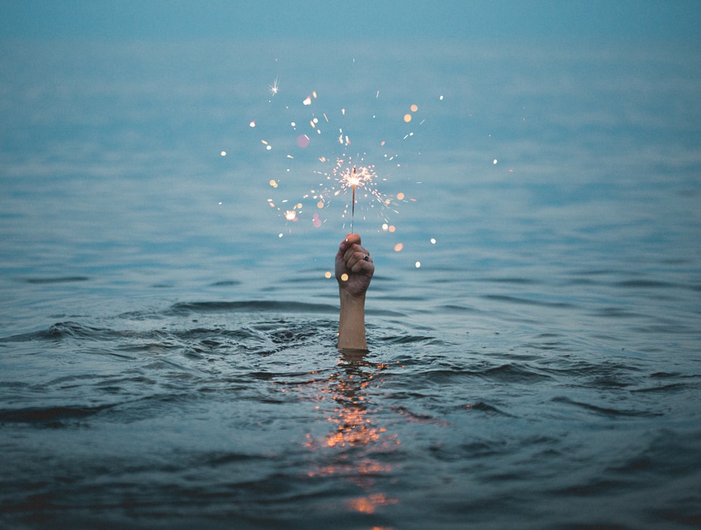 hand hold sparkler above the ocean